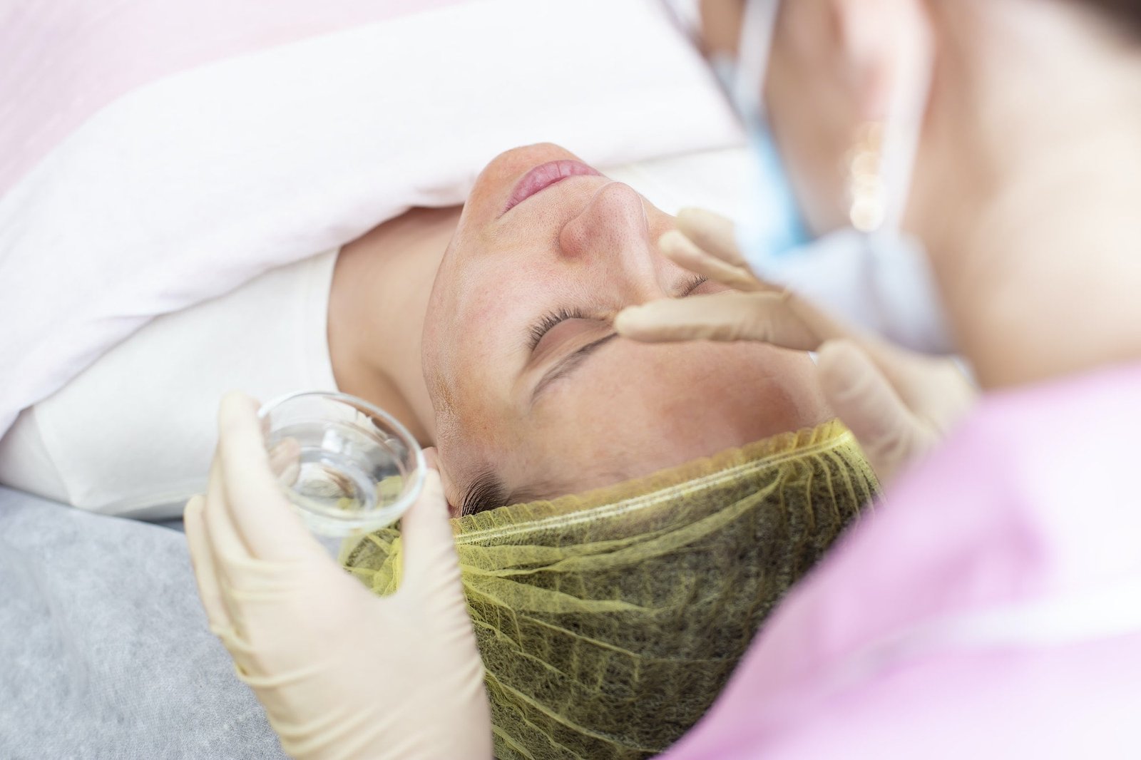A professional cosmetologist applies a chemical peeling solution to the patient on the face